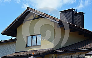 An outside view of an attic with stucco walls, clay, ceramic roof, two chimneys, roof gutters and an attic window with closed