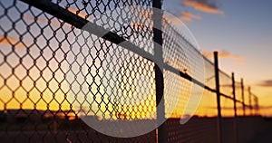 An Outside View of a Secure Area Enclosed by a Mesh Wire Fence with Barbed Wires at Sunset