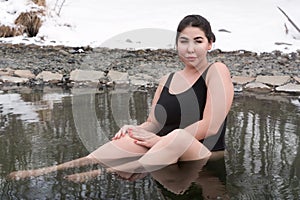 Outsize young adult woman in black swimming costume sitting and bathing in in outdoors pool at spa