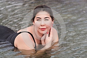 Outsize young brunette adult model in black bathing swimsuit lying down and relaxation in spa pool