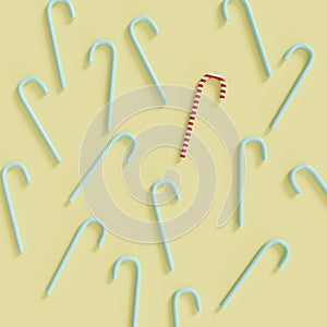 Outstanding red-white candy cane among blue candy canes on pastel yellow background