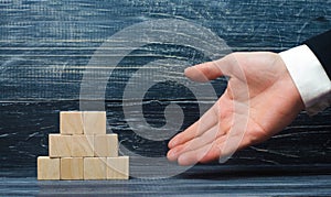 The outstretched hand of a businessman points to a pyramid of wooden squares. Concept promoter, sale and purchase of goods.