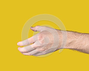 Outstretched male hand with open palm ready to shake other hand on yellow background. Gesture to reach out or take something.