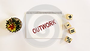 OUTWORK , the text is written on a notebook and a white background. On the table are wooden cubes with signs and there is a cactus