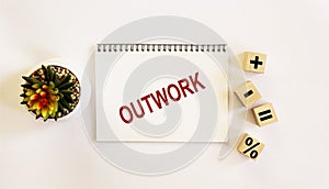 OUTWORK , the text is written on a notebook and a white background. On the table are wooden cubes with signs and there is a cactus photo