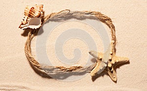 Oval frame of rope with starfish and seashell on sand