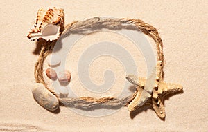 Oval frame of rope, starfish, seashell and stones on sand