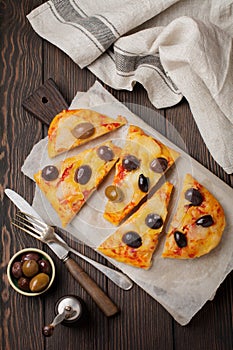 Oval Greek pizza with olives and tomato cut into pieces on dark wooden rustic background. Selective focus. Top view. Copy space