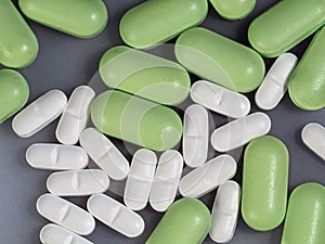 Oval green and white pills in bulk on a gray background. Close-up. Medical background with medications. View from above.