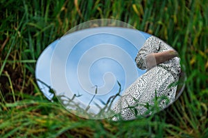 An oval mirror lies on the grass and reflects the waist of a girl.