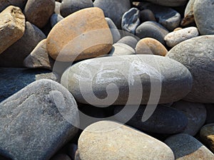 Oval stones, large smooth sea pebbles, illuminated by the summer sun. The word sea is written on the stone. Summer
