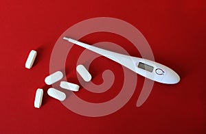 Oval white biconvex tablets and white digital thermometer on red background with light shadows.  Antipyretics concept