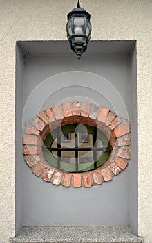 Oval window lined with brick and grate with reflection and lamp above it