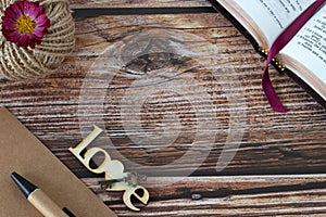 ove wooden text with heart, old key, open holy bible book, pen and vintage paper on rustic table with copy space, top view