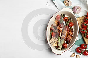 Oven baked asparagus wrapped with bacon in ceramic dish on white wooden table. Space for text