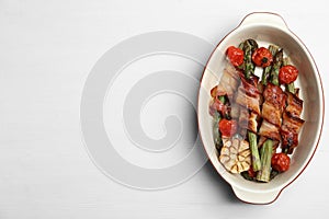Oven baked asparagus wrapped with bacon in ceramic dish on white table, top view. Space for text