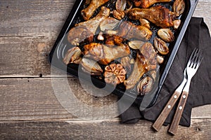 Oven baked chicken legs with onions, garlic and peppers on a dark wooden background closeup. Top view with copy space. Wooden rust