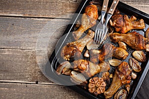 Oven baked chicken legs with onions, garlic and peppers on a dark wooden background closeup. Top view with copy space