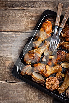 Oven baked chicken legs with onions, garlic and peppers on a dark wooden background closeup. Top view with copy space