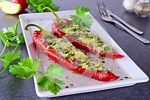 Oven cooked red paprika stuffed with cheese, garlic and herbs on a white plate with parcley and cherry tomatoes an photo