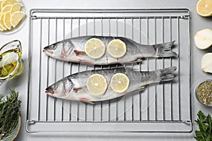Oven rack with raw sea bass fish and ingredients on light grey table, flat lay