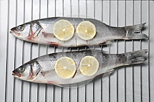 Oven rack with raw sea bass fish and lemon on light grey table, top view