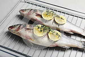 Oven rack with raw sea bass fish, lemon and thyme on light grey table, closeup