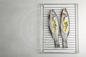 Oven rack with raw sea bass fish, lemon and thyme on light grey table, top view. Space for text