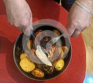 Oven roasted chicken with potatoes and male hands that cut the meat