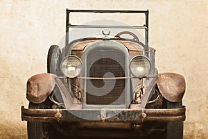 Over a century old rusted and broken classic car in front of an old wall