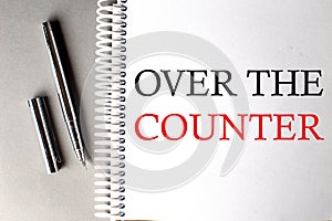 OVER THE COUNTER text on a notebook with pen on grey background