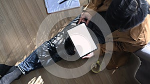 Over head shot of man freelancer sitting on floor and using digital tablet with blank screen.