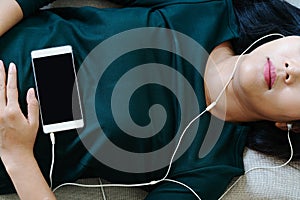 Over head view of beautiful young woman laying down on sofa using smartphone to listen the music