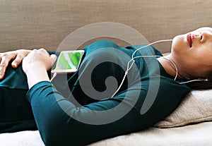 Over head view of beautiful young woman laying down on sofa using smartphone to listen the music