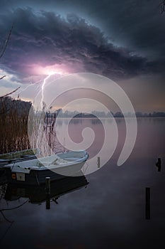 Over the lake with a rowing boat rages a thunderstorm with lightnings