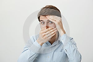 Is it over now. Portrait of scared and shocked young attractive man covering face with hands as if hiding or feeling