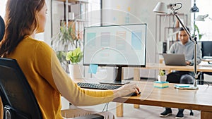 Over the Shoulder: Female Mobile Software Developer Sitting at Her Desk Using Desktop Computer wit
