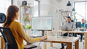 Over the Shoulder: Female Mobile Software Developer Sitting at Her Desk Using Desktop Computer wit