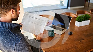 Over the shoulder image of man holding newspaper at home