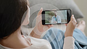 Over shoulder mobile screen view female patient woman talks remotely with medic provides online medical education from