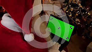 Over the shoulder modern Santa Claus uses laptop with green screen markers