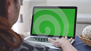 Over the shoulder shot of Asian woman looking at green screen. Office person using laptop computer with laptop green screen, 4K do