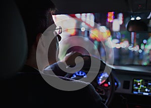 Over the shoulder view of businessman driving at night in the city, illuminated city lights