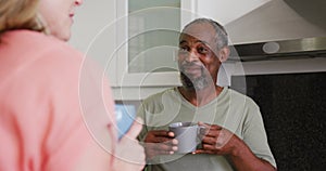 Over shoulder view of diverse senior couple drinking coffee smiling and talking in kitchen