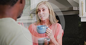Over shoulder view of diverse senior couple drinking coffee and talking in kitchen
