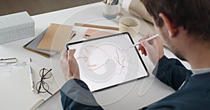 Over shoulder view of fmale artist drawing illustration on tablet while sitting at workplace. Graphic illustrator using