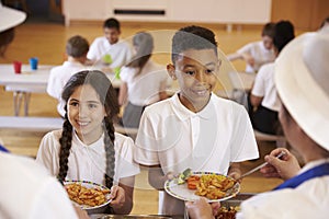 Over shoulder view of kids being served in school cafeteria photo
