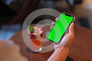 Over the shoulder view of man hand holding green screen smart phone in bar