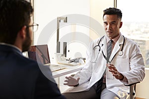 Over The Shoulder View Of Man Having Consultation With Male Doctor In Hospital Office