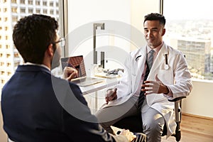 Over The Shoulder View Of Man Having Consultation With Male Doctor In Hospital Office